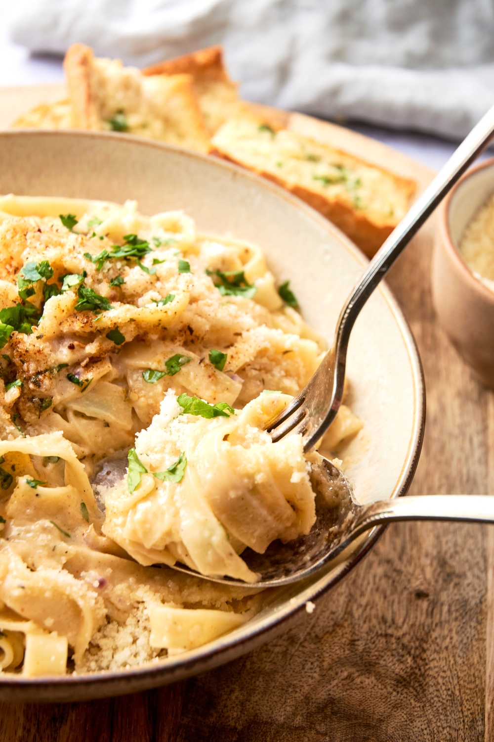 Someone twirls fettuccine and Cajun alfredo sauce on a fork in a white bowl full of fettuccine and Cajun Alfredo sauce.