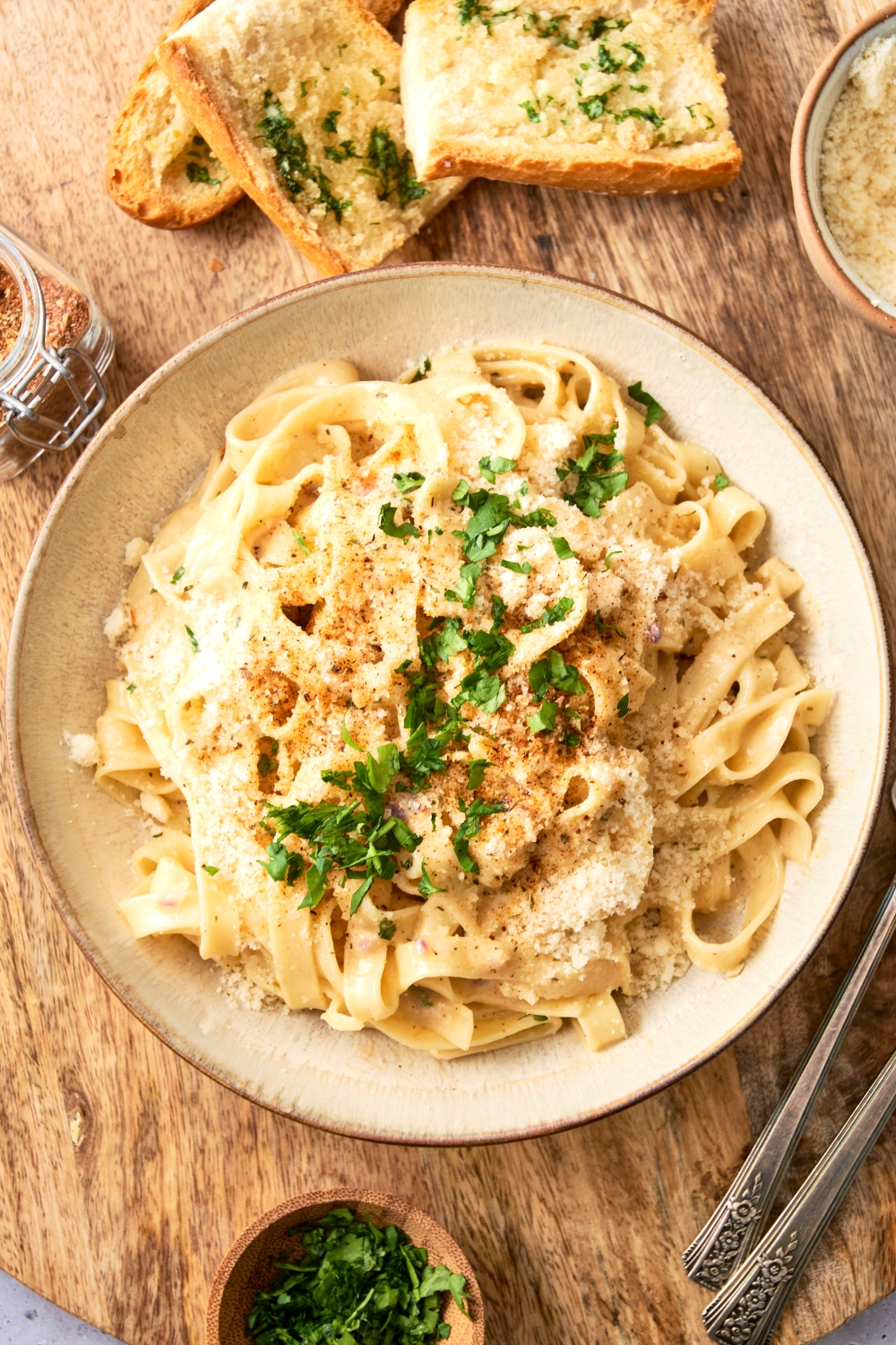 A white bowl is full of fettuccine Alfredo topped with fresh herbs and extra cheese.