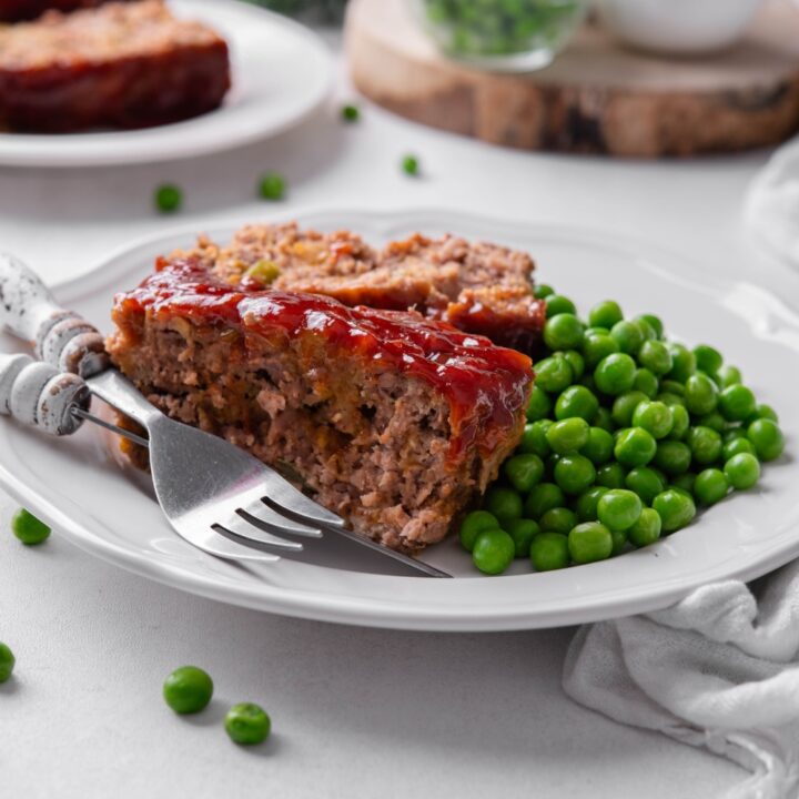 A plate with the meatloaf served with peas.