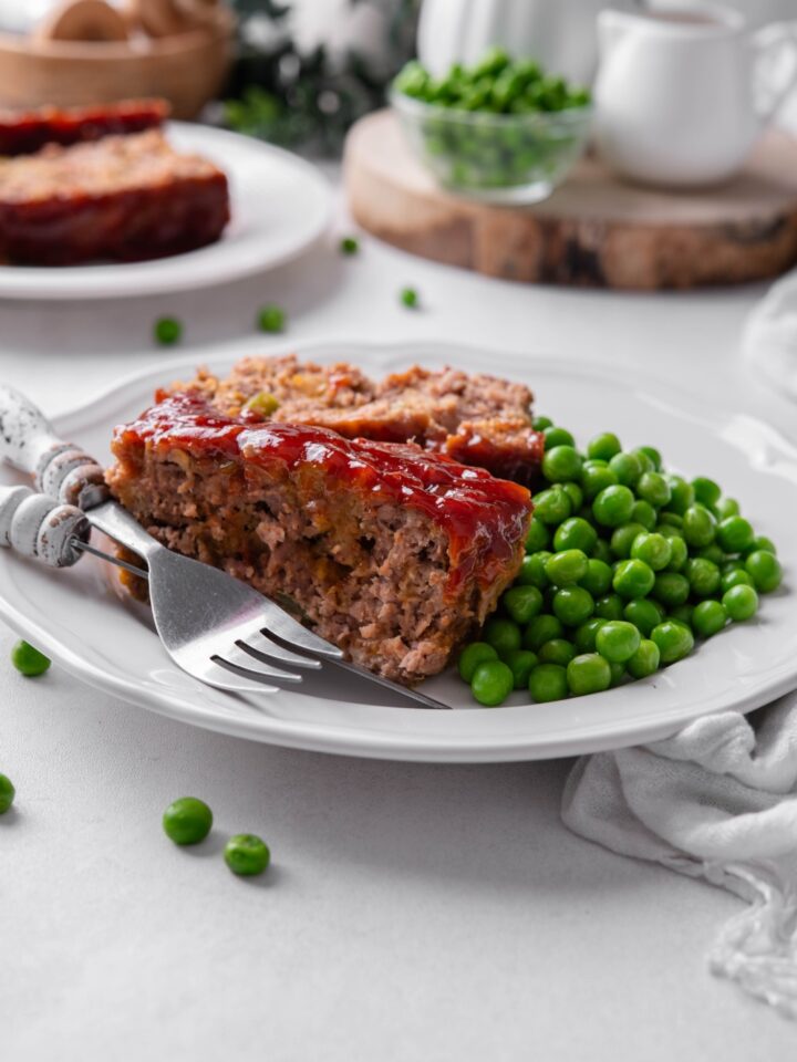 A plate with the meatloaf served with peas.