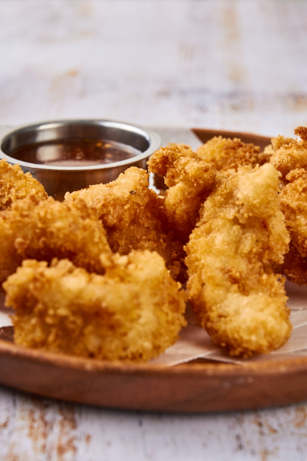 Golden brown shrimp are on a red plate. There is also a cup of sauce on the plate.