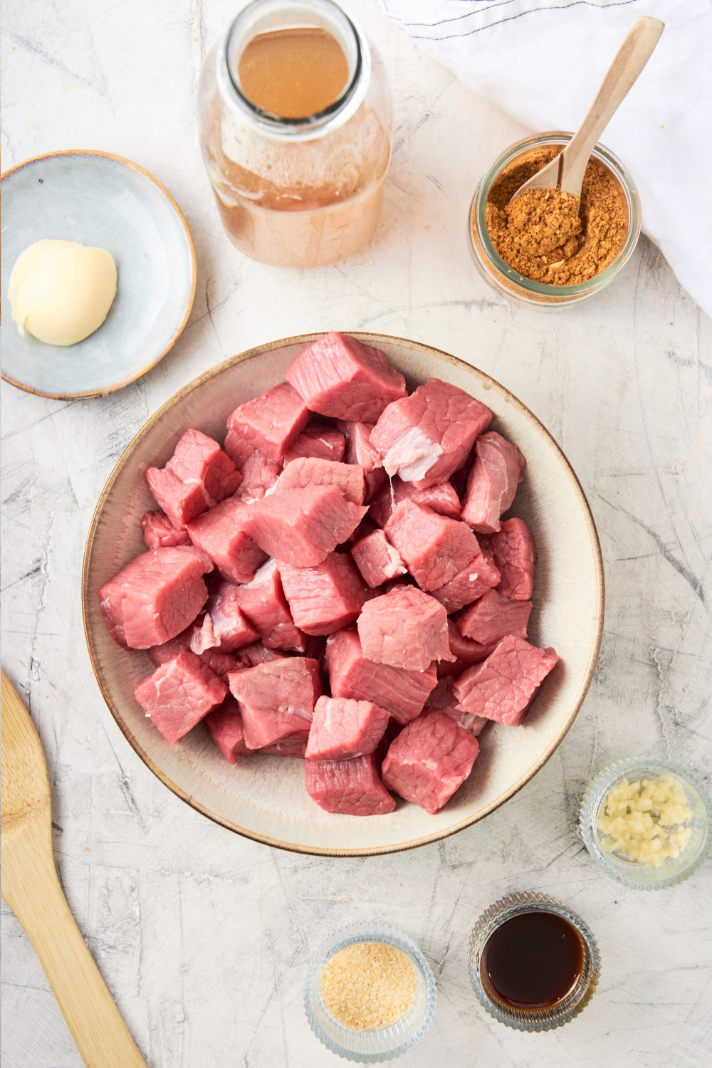 Gravy mix, raw beef, broth, butter, garlic, onion powder, and Worcestershire sauce are all in separate bowls on a marble countertop.