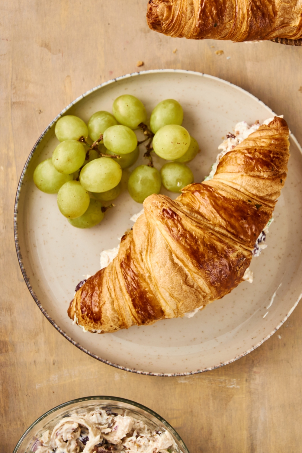 A gray plate holds a bunch of grapes and a completed chicken salad croissan.