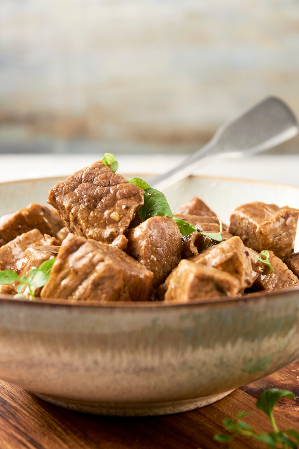 A bowl is full of beef tips, fresh herbs, and gravy. A spoon rests in the background.