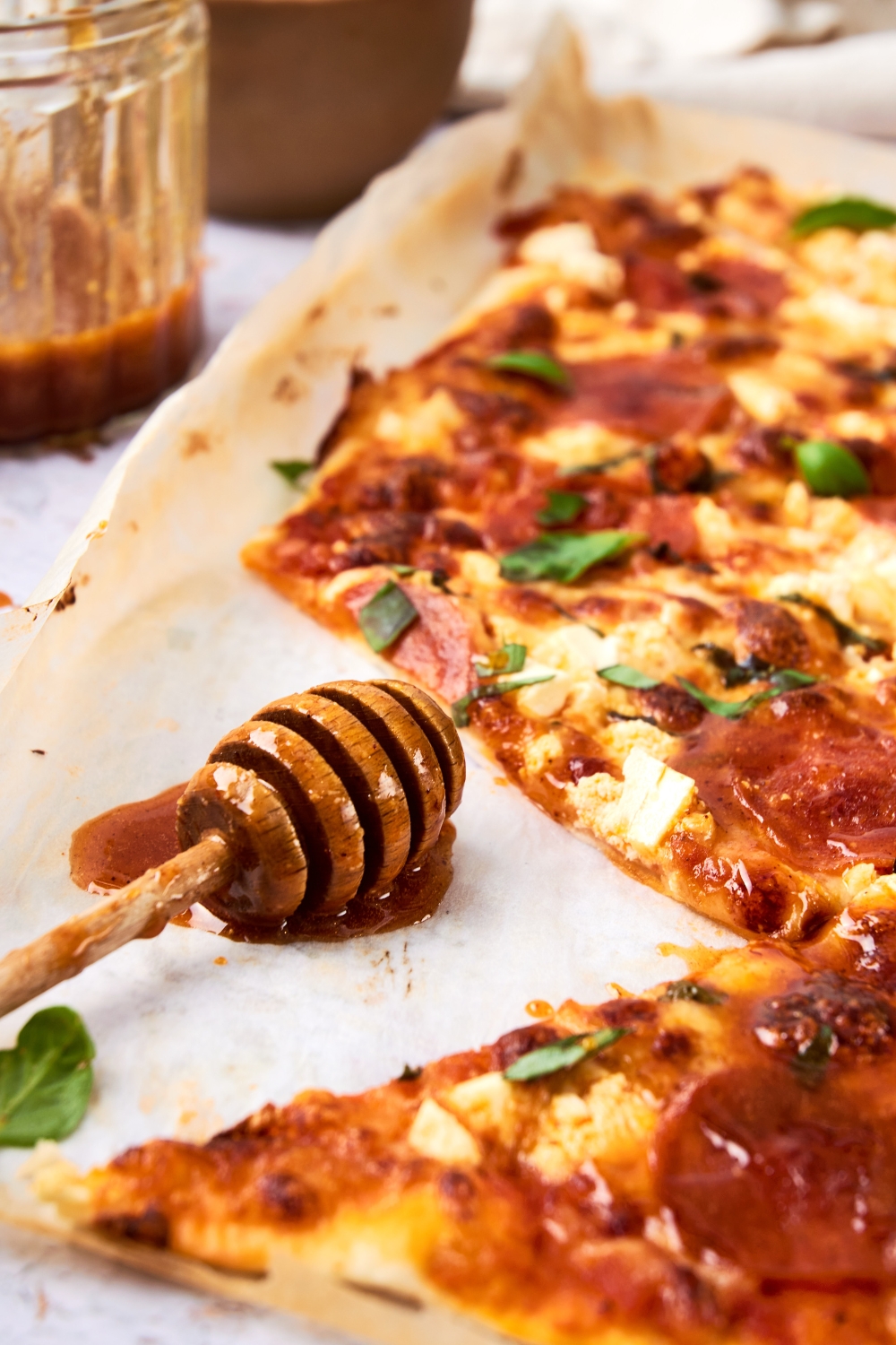 A honey dipper is resting on a parchment paper next to a cooked hot honey pizza.