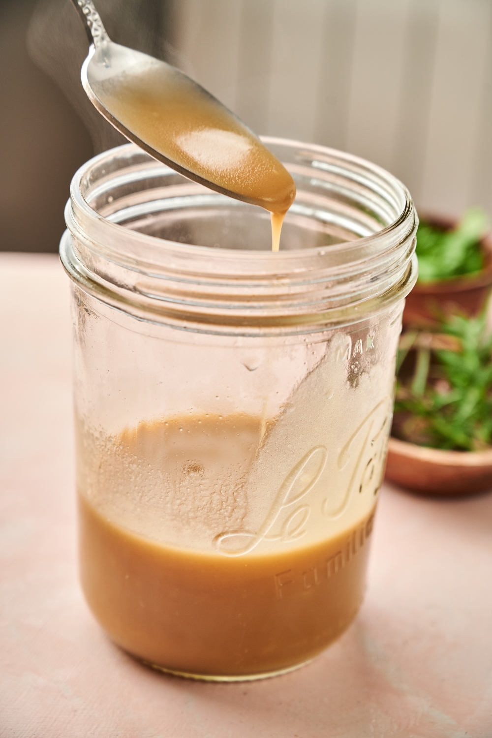 Someone drips pork gravy from a spoon into a glass jar.