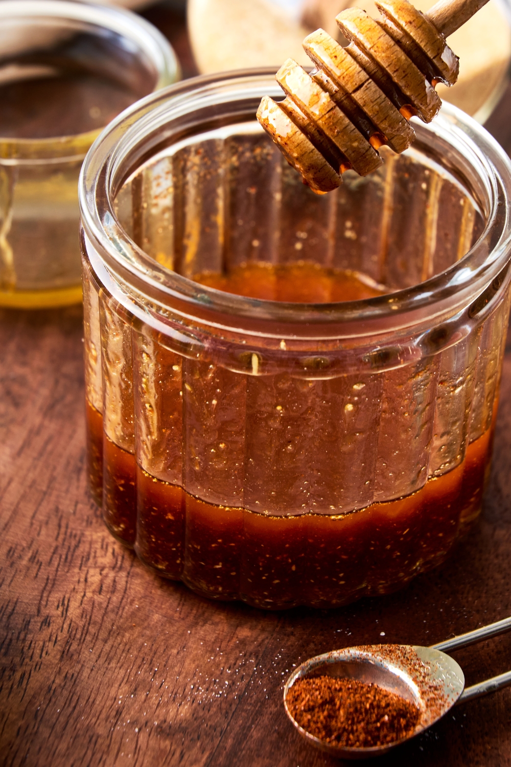 A honey dipper is held above a glass jar of hot honey.