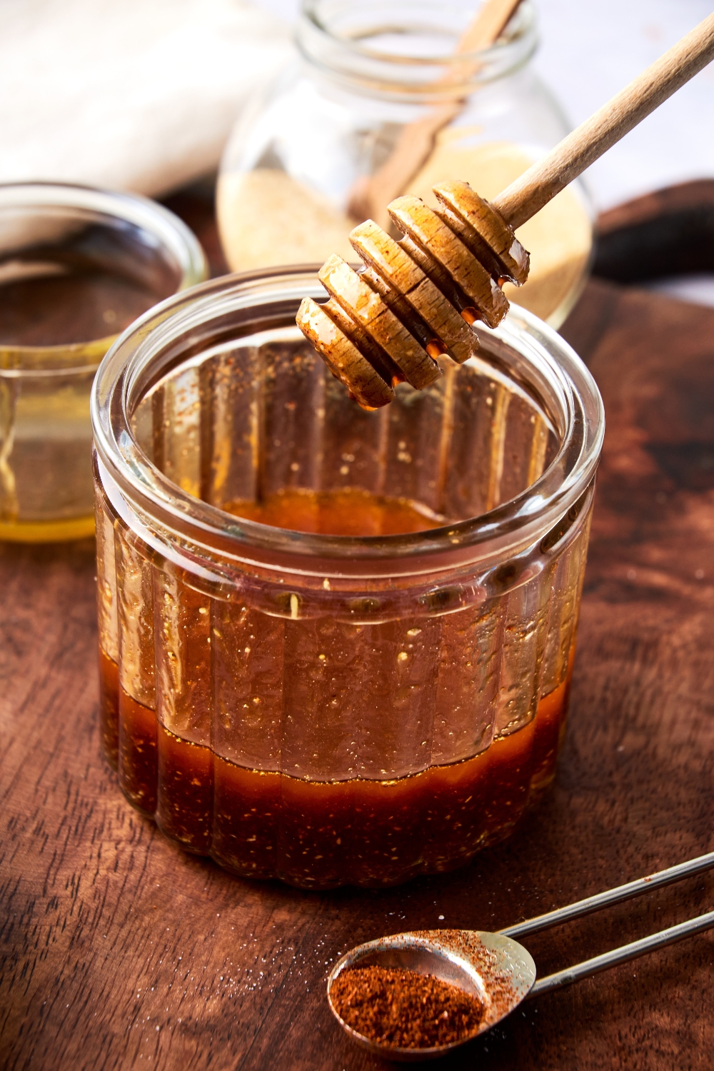 Someone holds a honey dipper over a glass jar full of hot honey.
