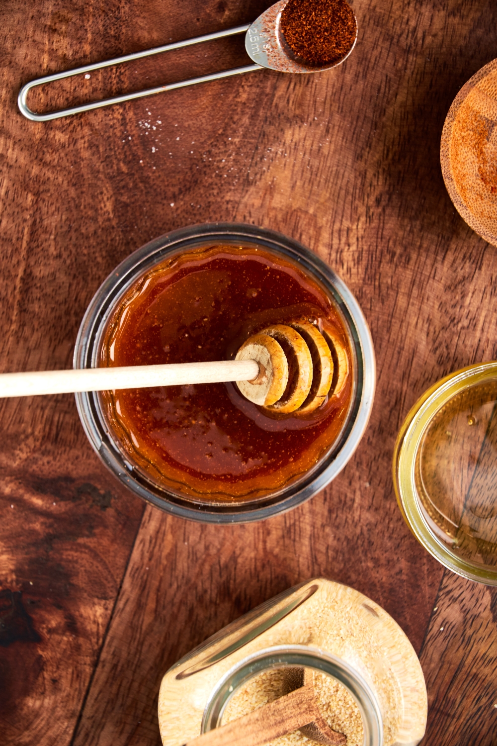 A honey dipper rests in a glass jar full of hot honey.