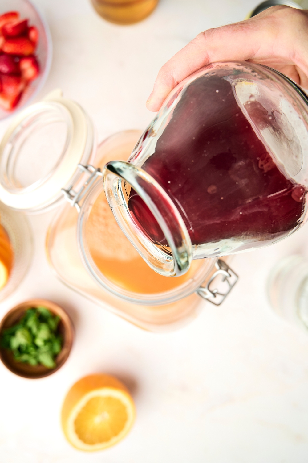 Someone pours cranberry juice into a large pitcher full of orange juice and fruit punch.