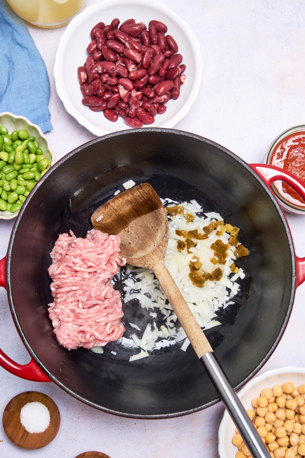 A wooden spoon rests in a large pot of ground turkey, onion, and jalapenos.