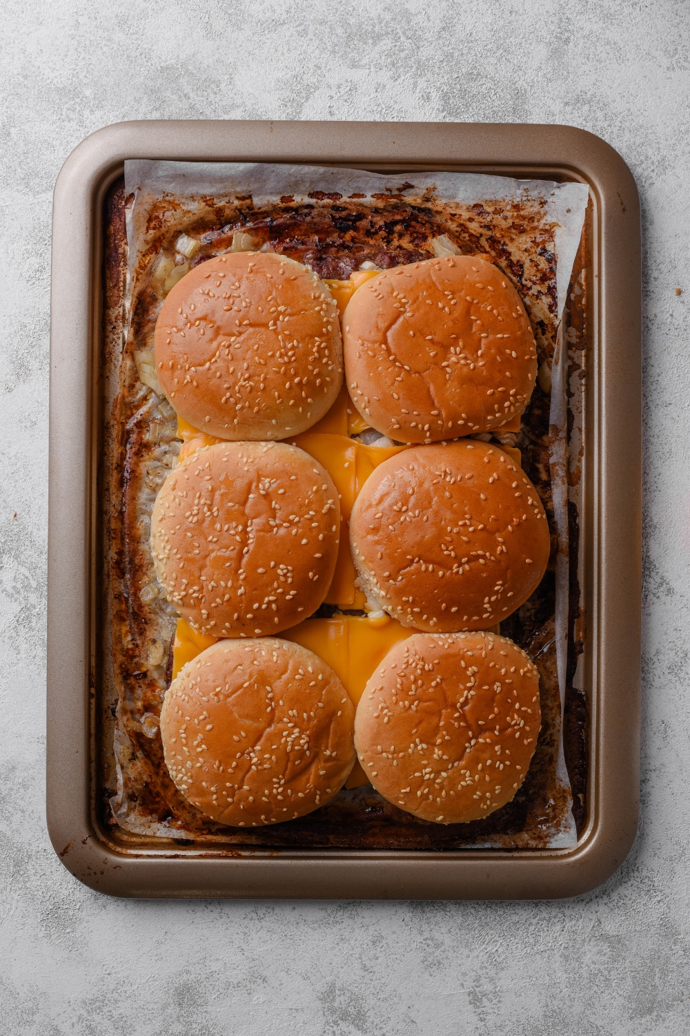 A parchment paper lined baking tray holds white castle sliders with top buns.