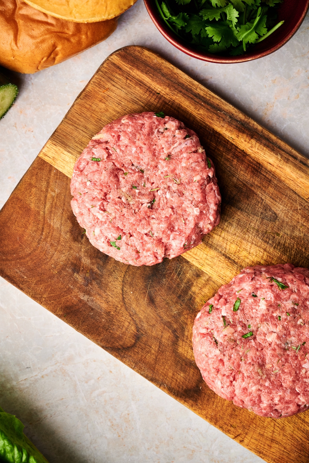 Two patties of raw lamb are formed into circles on a wooden cutting board.