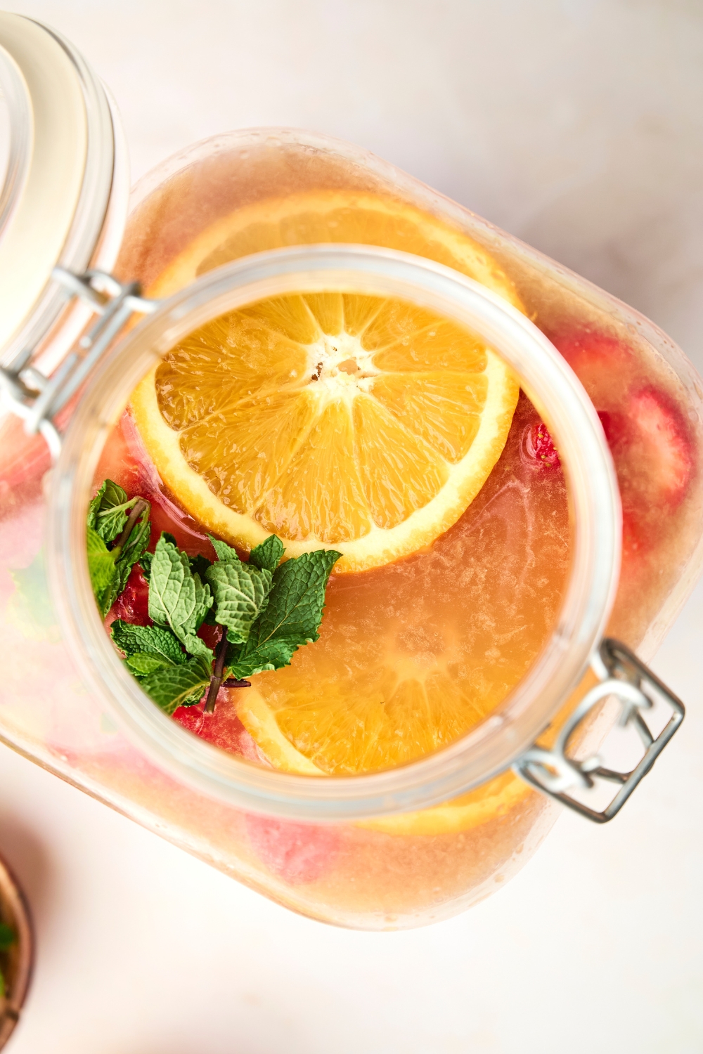 A large glass jar is full of jungle juice, orange slices, and mint.