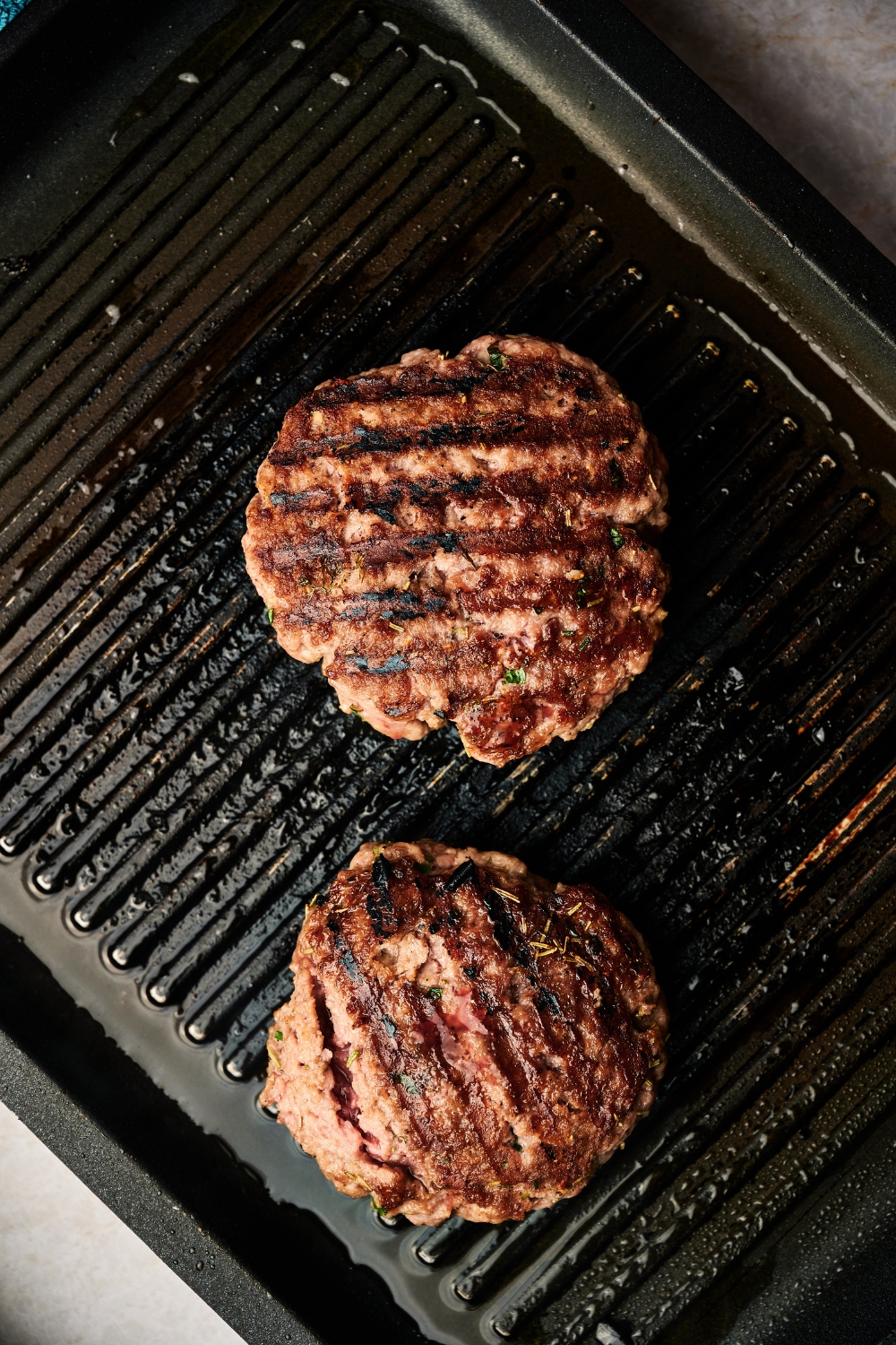 Two lamb patties are on a grill pan. Each patty has dark grill marks.