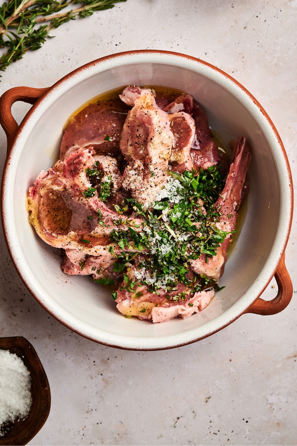 A large pot is full of raw lamb, salt, and fresh herbs.