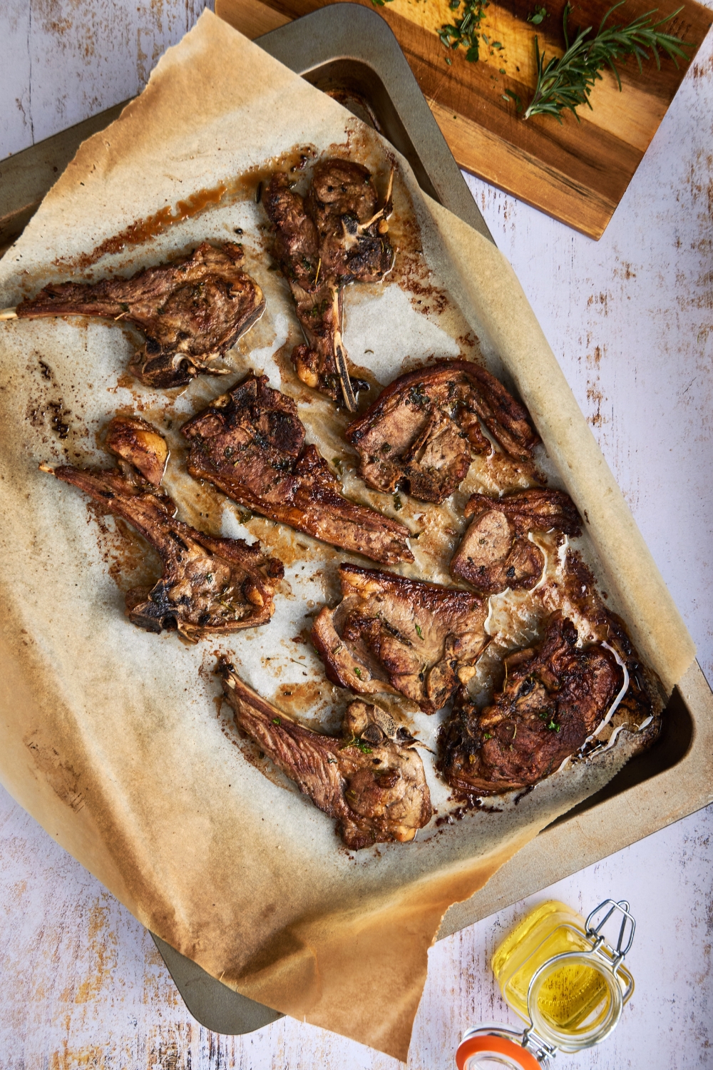 A baking tray is lined with parchment paper and holds oven baked lamb shoulder chops.