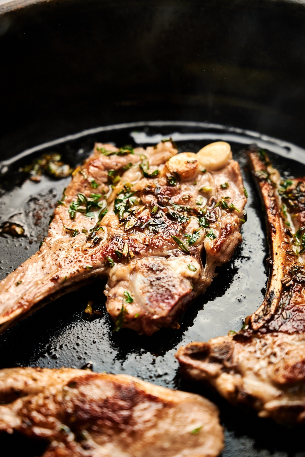 Lamb lollipops are searing in oil in a black cast iron pan.