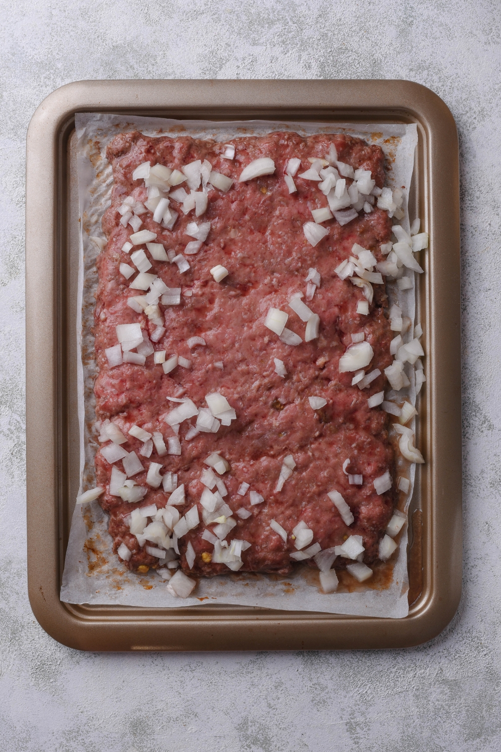 A baking tray with hamburger and diced onions sits on a gray counter.