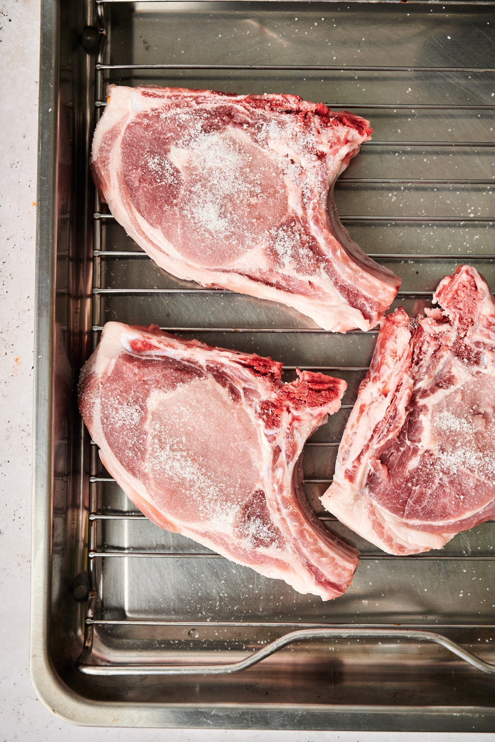 Raw pork chops sit on a wire rack over top of a baking tray.