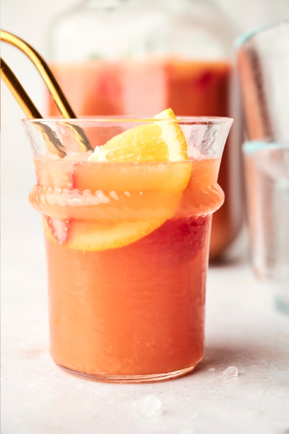 A small glass of jungle juice has an orange slice and two golden straws in it.
