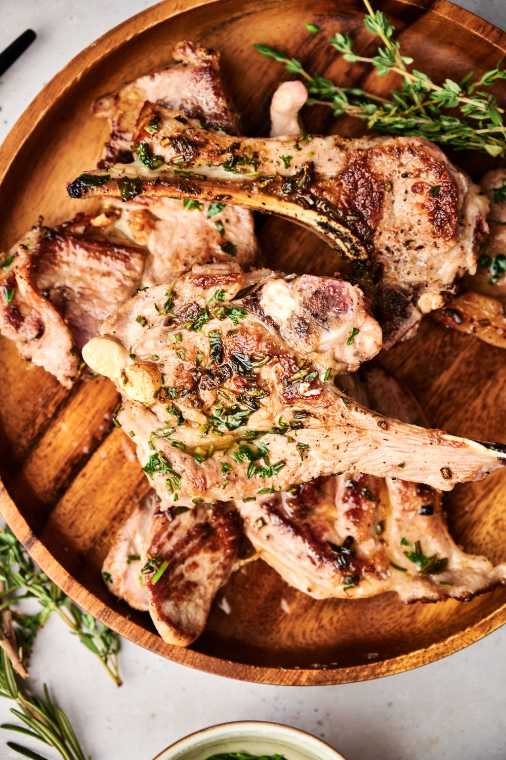 A wooden serving board piled with seared lamb lollipops.