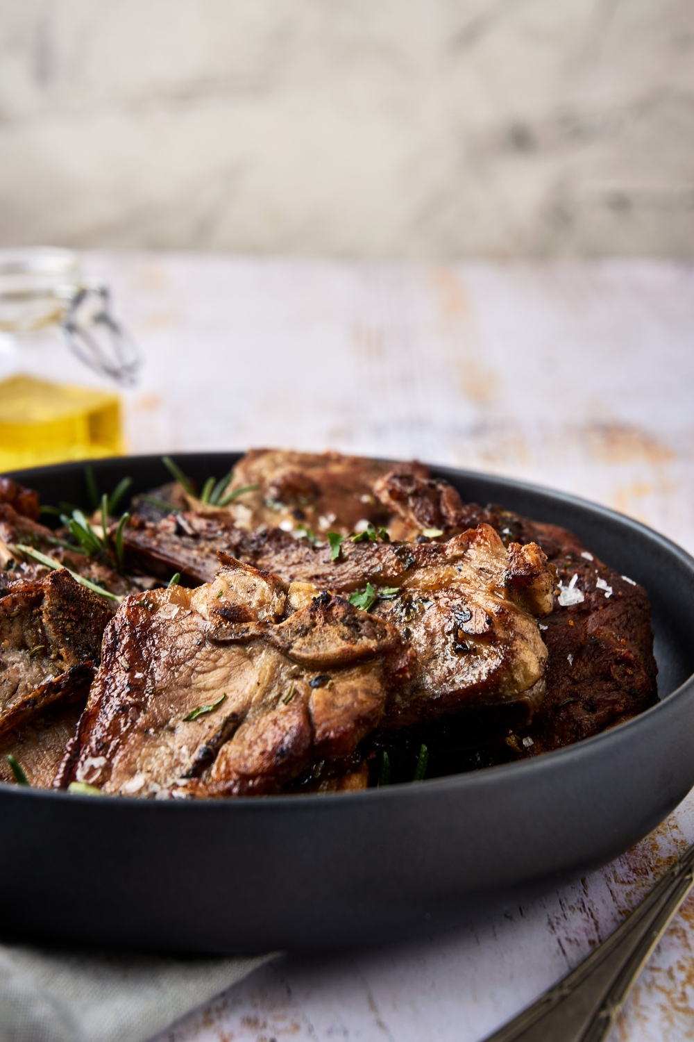 A black dish is full of lamb shoulder chops. The chops are garnished with fresh herbs.
