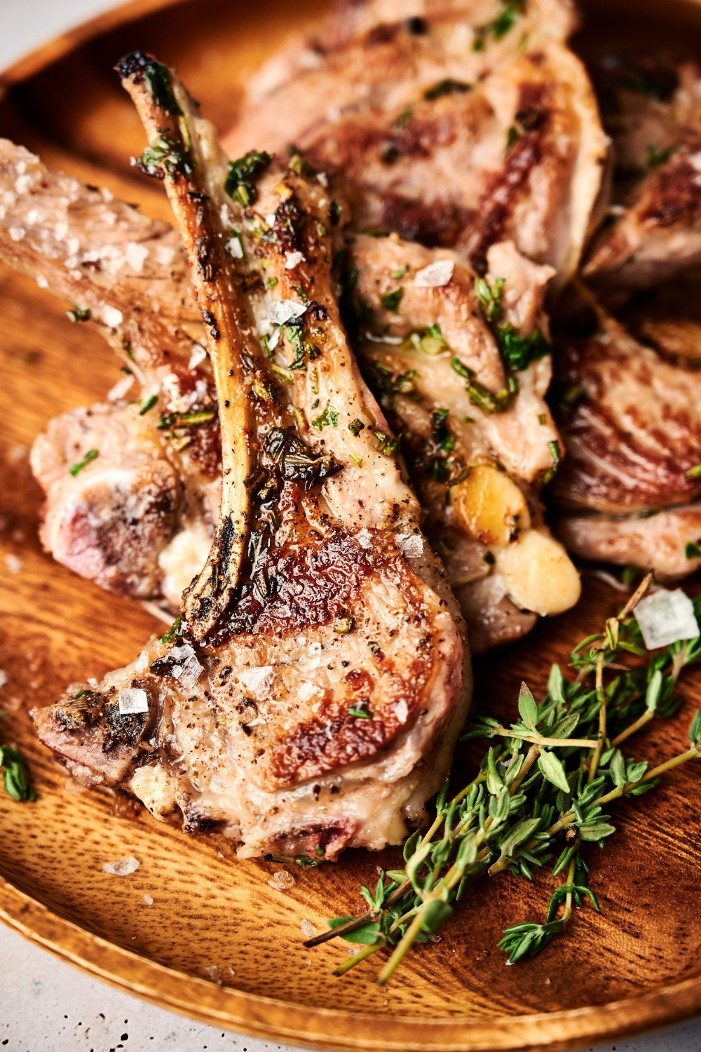 A seared lamb lollipop sits atop other lamb lollipops on a wooden serving board.