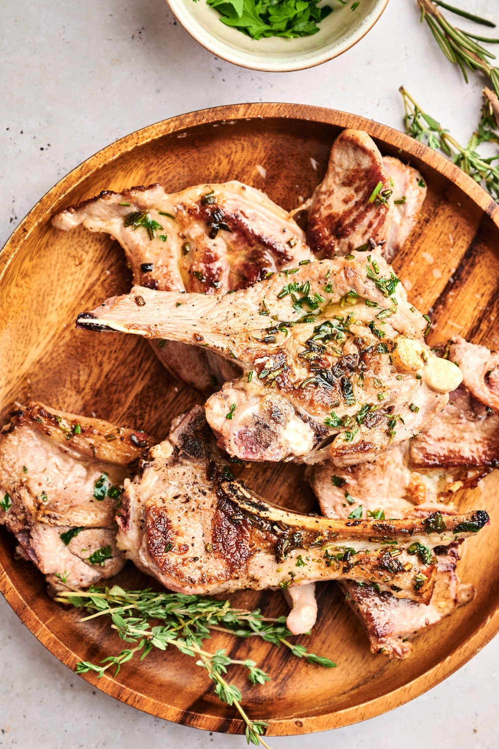 A wooden serving board is full of lamb lollipops and fresh herbs.