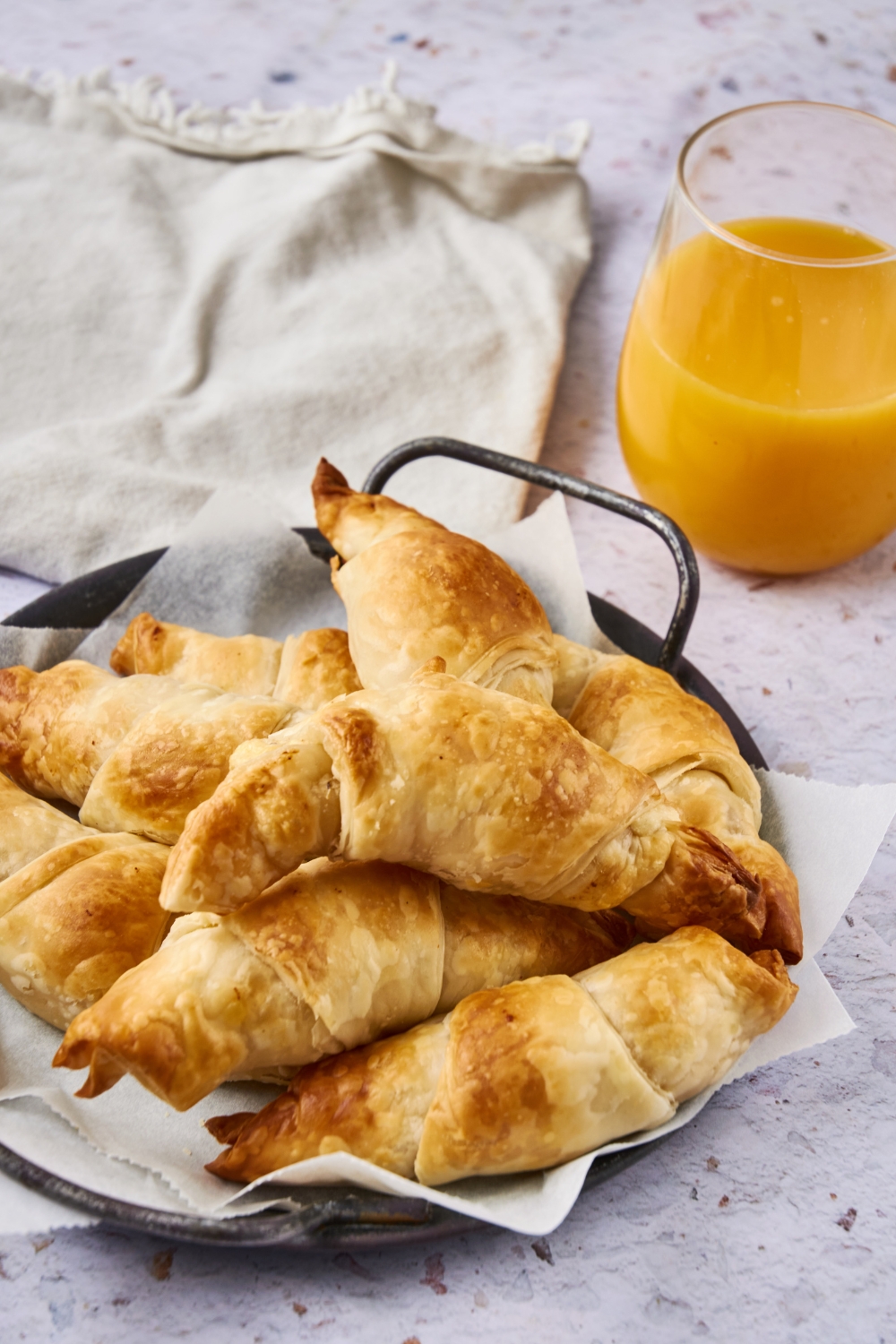 A platter of sausage cream cheese crescents is on a counter. A glass of orange juice is near by.