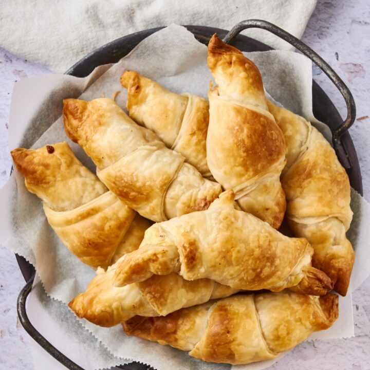 A platter or sausage cream cheese crescents is on a white counter. A glass of orange juice is next to it.