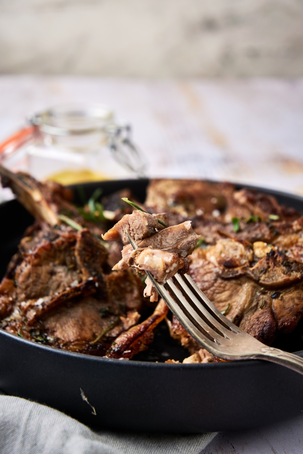 A black dish is full of cooked lamb shoulder chops. A fork rests on the side of the dish.