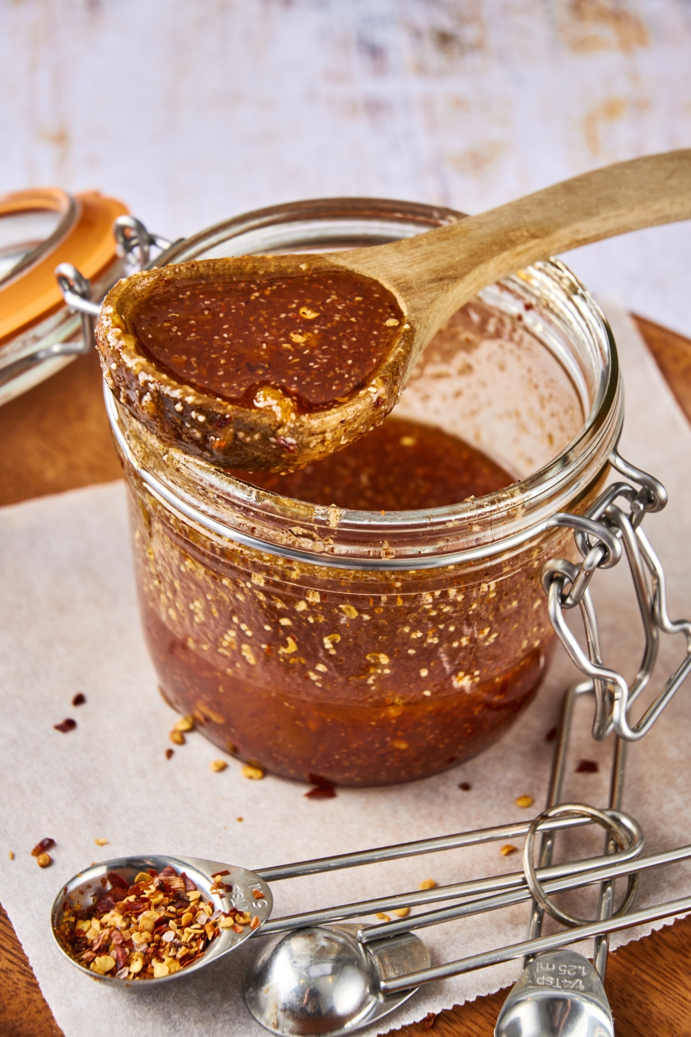 A wooden spoon covered in sauce rests on an open jar of Popeye's sweet heat sauce.
