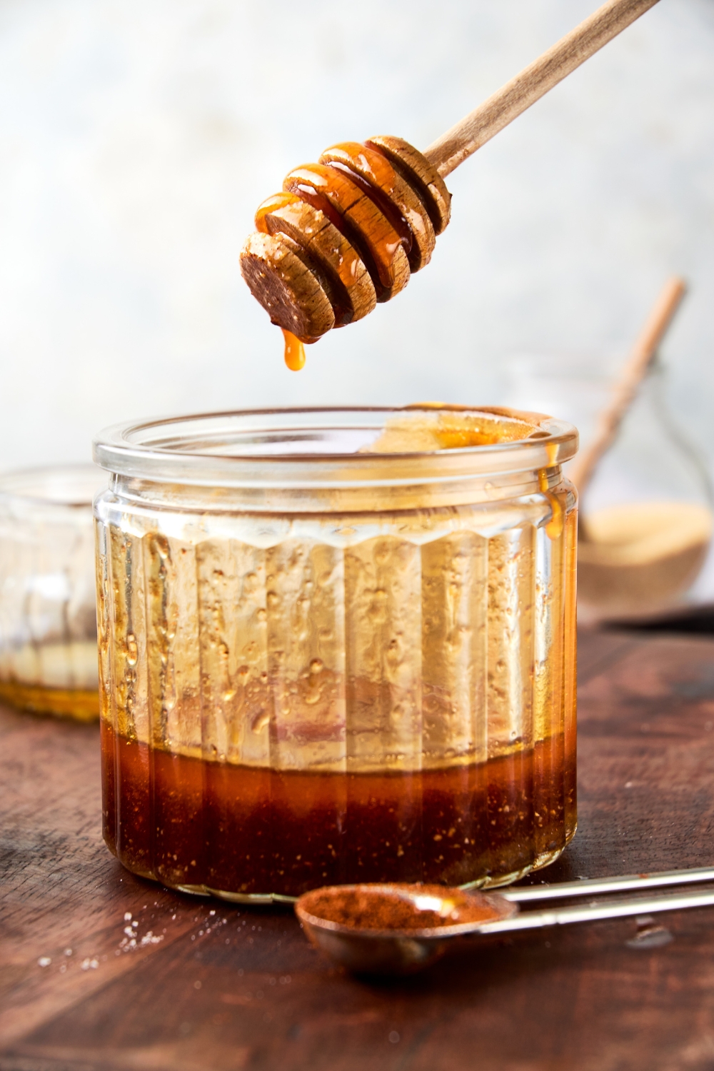 Someone holds a honey dipper over a glass jar full of hot honey.