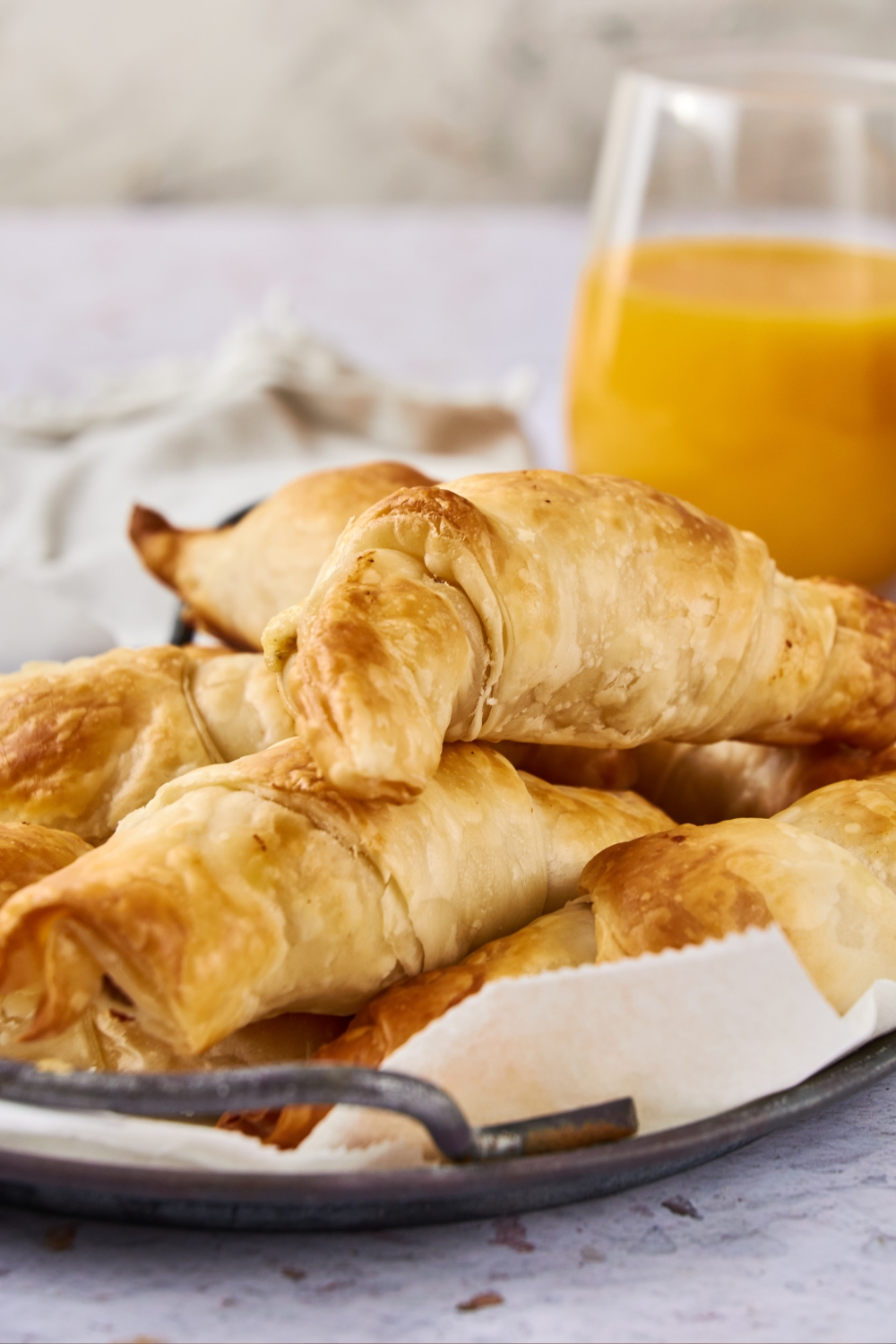 A platter of crescents piled high is on a white counter. A glass of orange juice is next to it.