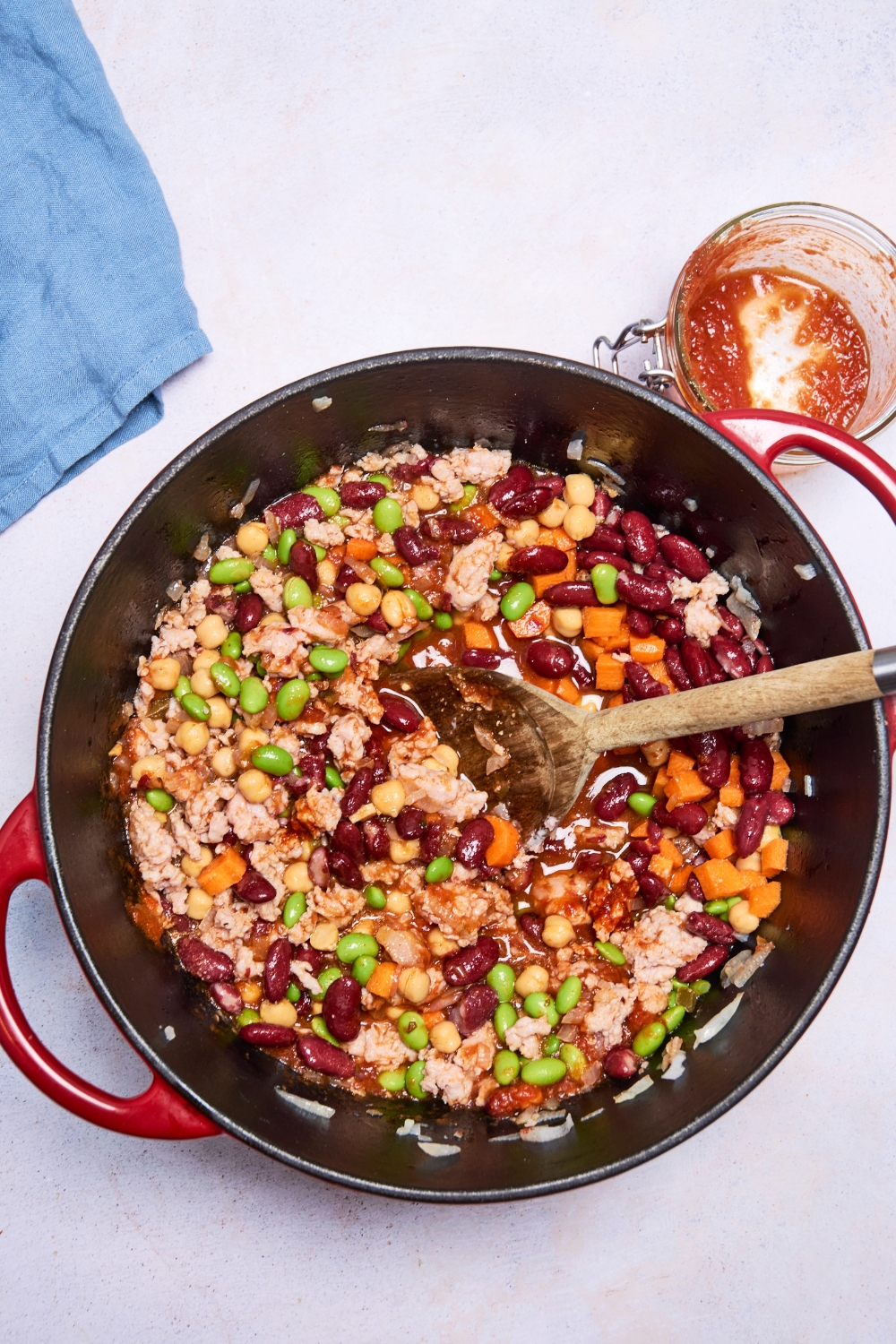 A pot is full of turkey chili. A wooden spoon mixes the ingredients in the pot.