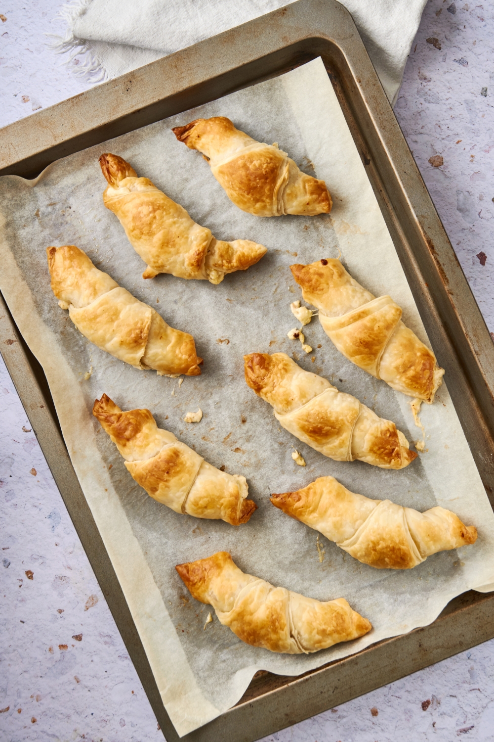 A baking tray lined with parchment pepper holds eight sausage cream cheese crescents. They're golden brown.