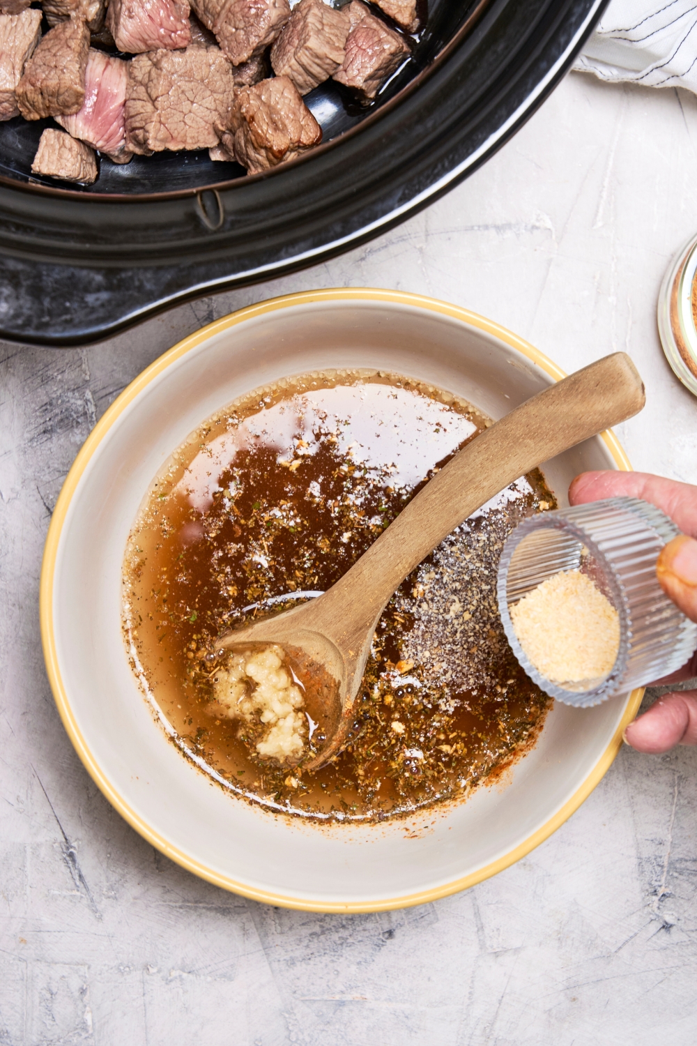 Someone adds onion powder to a bowl with gravy mixture in it. A wooden spoon rests in the bowl.