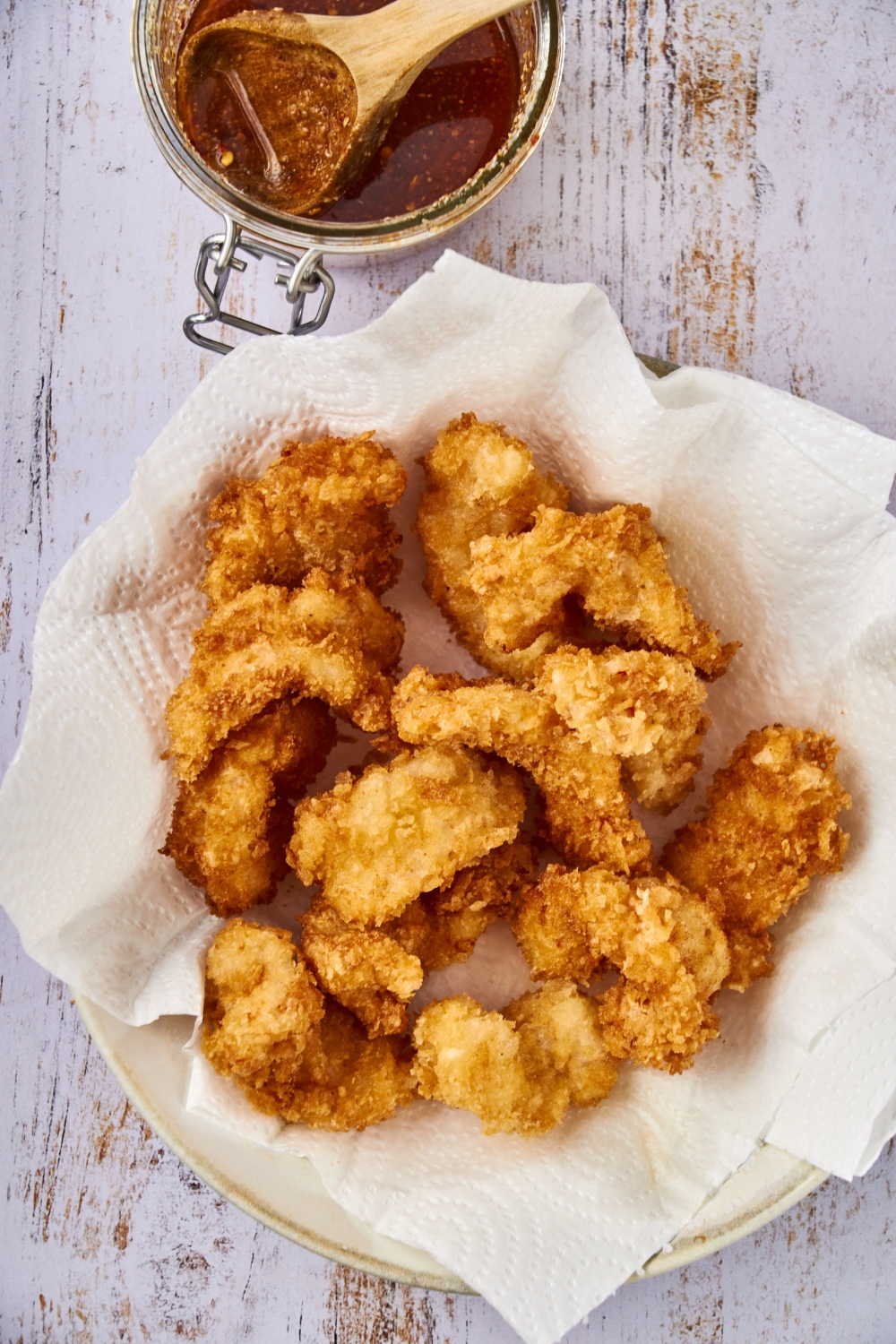 Golden brown shrimp are resting on a plate lined with paper towels.