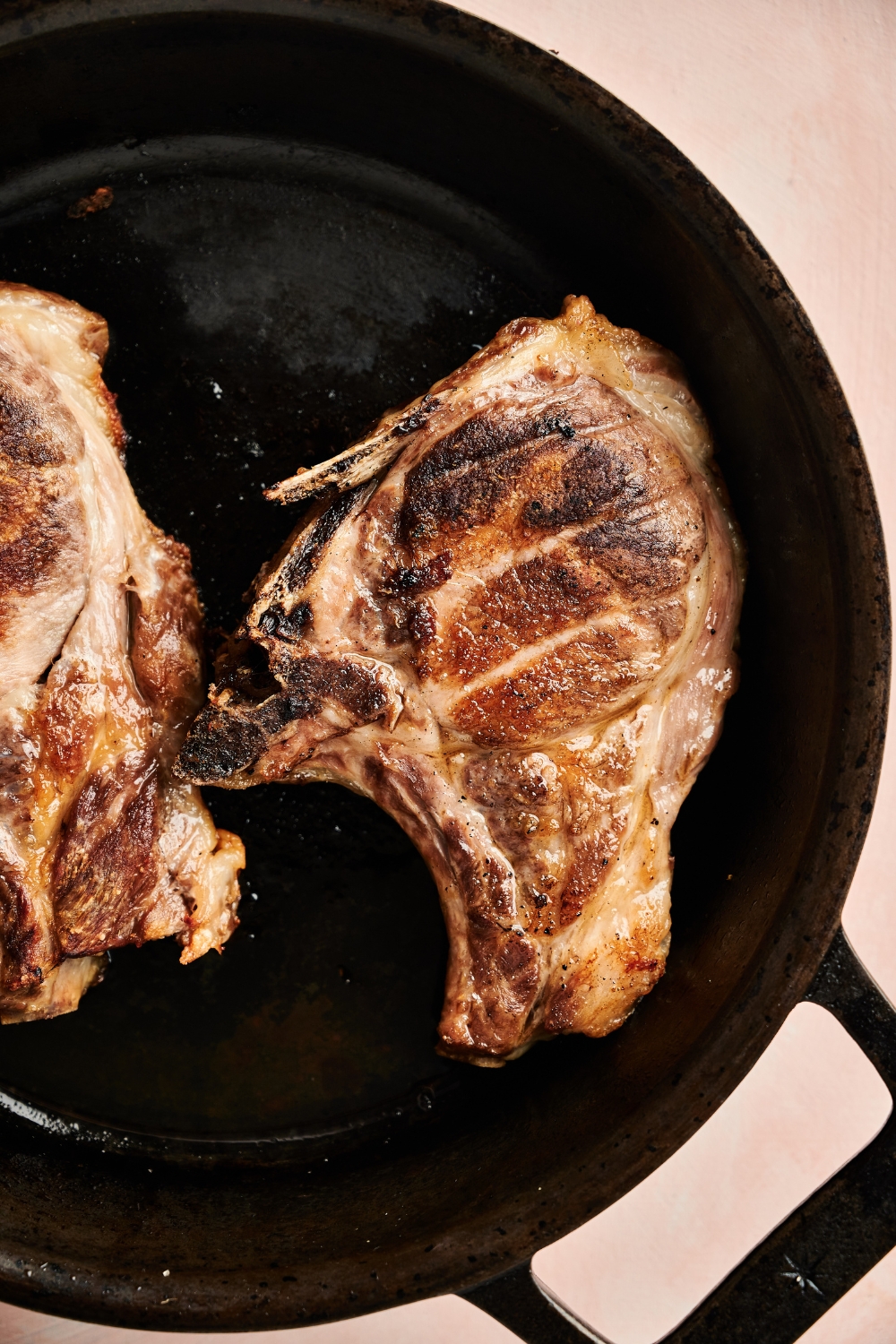 Two pork chops are in a black cast iron skillet. They are a golden brown color.