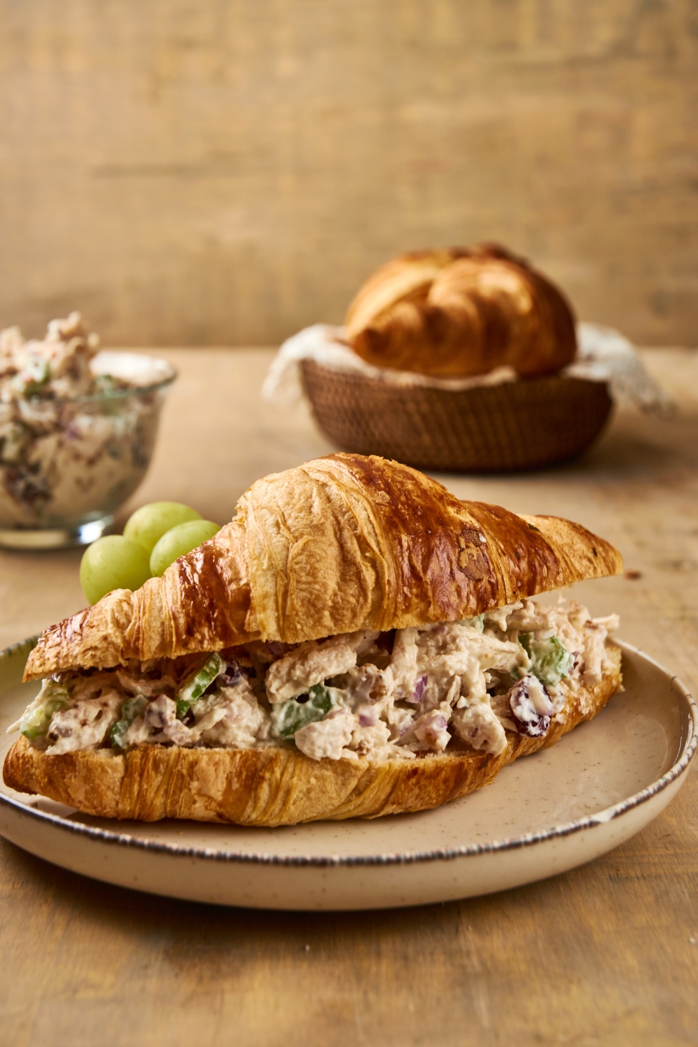 A chicken salad croissant sits on a gray plate. A few grapes are visible on the plate as well.