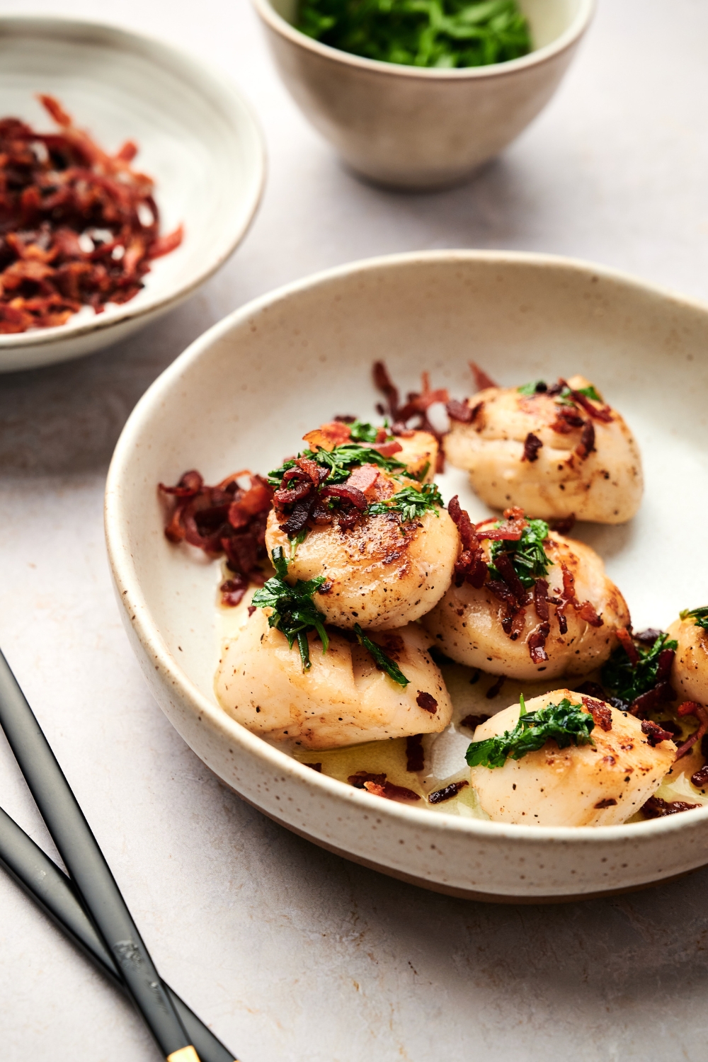 A bowl with cooked scallops topped with parsley and crispy bacon.