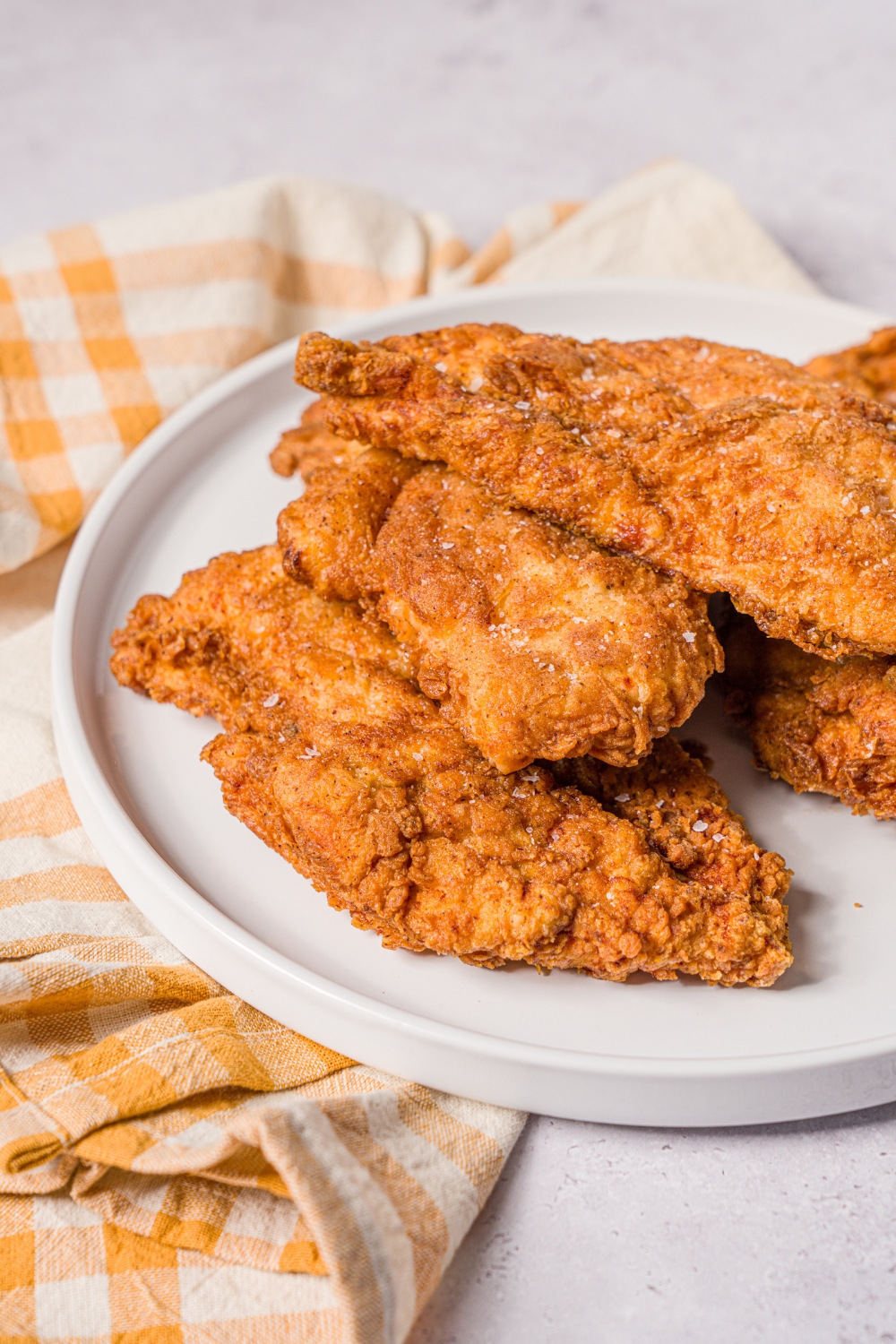 Part of a white plate with a few pieces of crispy fried chicken breast overlapping one another on the plate.