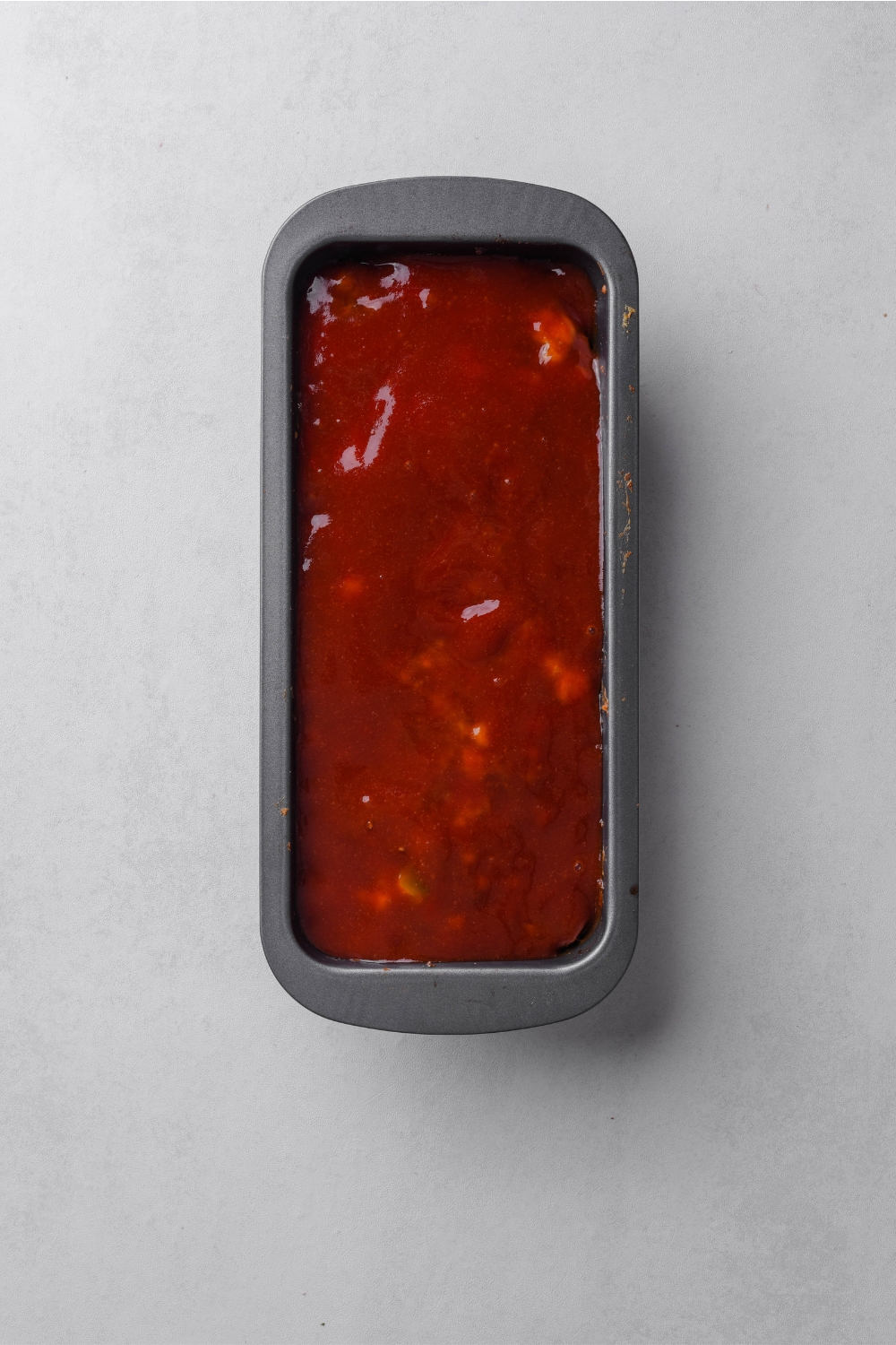 A loaf pan with the meatloaf and glaze added on top.