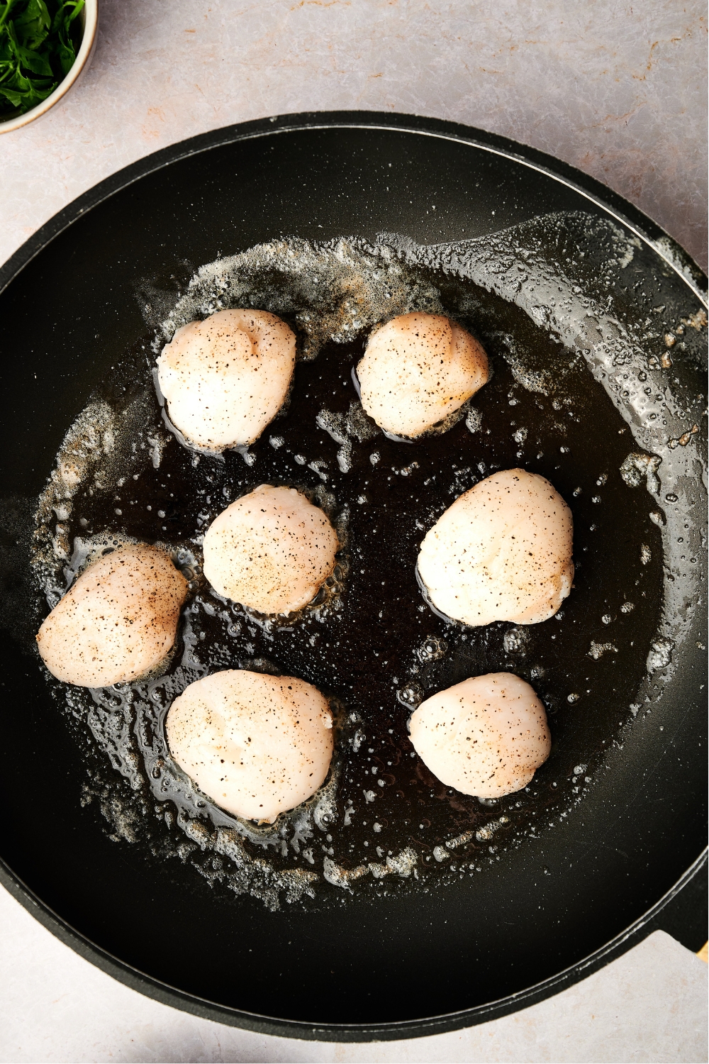 A frying pan with scallops cooking in butter.