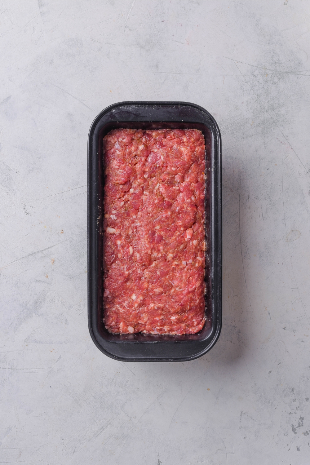 A meatloaf pan with the ground beef mixture in it.