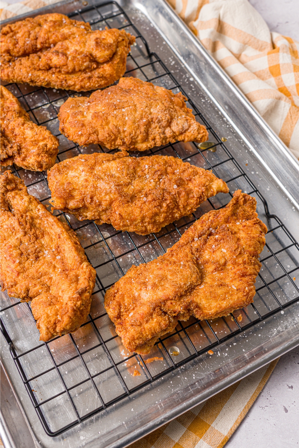 A bunch of pieces of fried chicken breasts on a wire rack on top of a baking sheet.