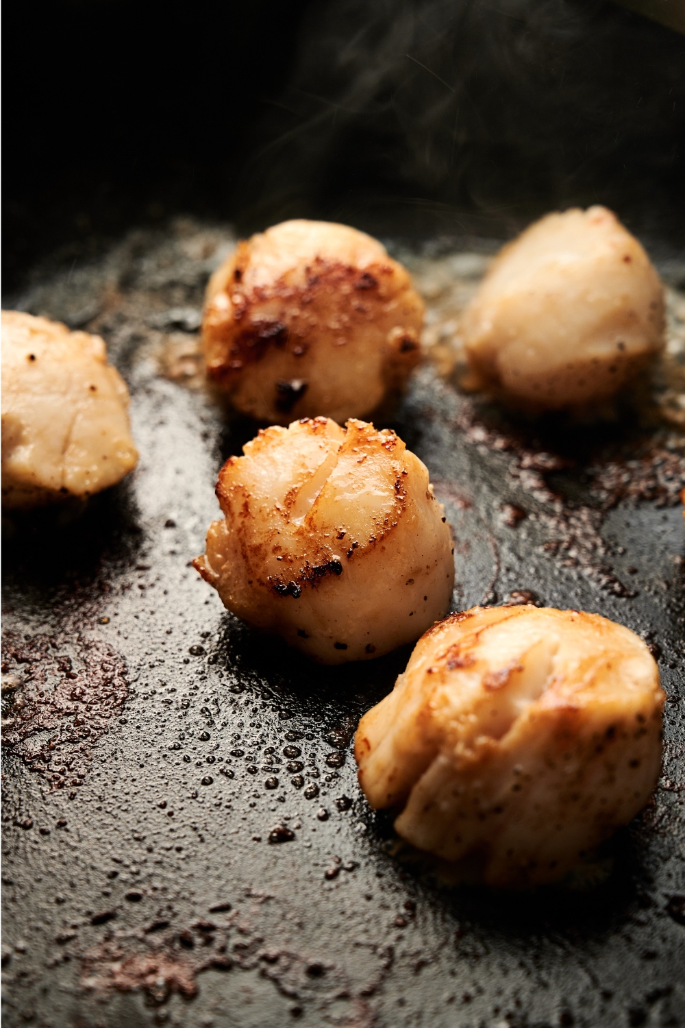 A frying pan with golden brown scallops cooking.