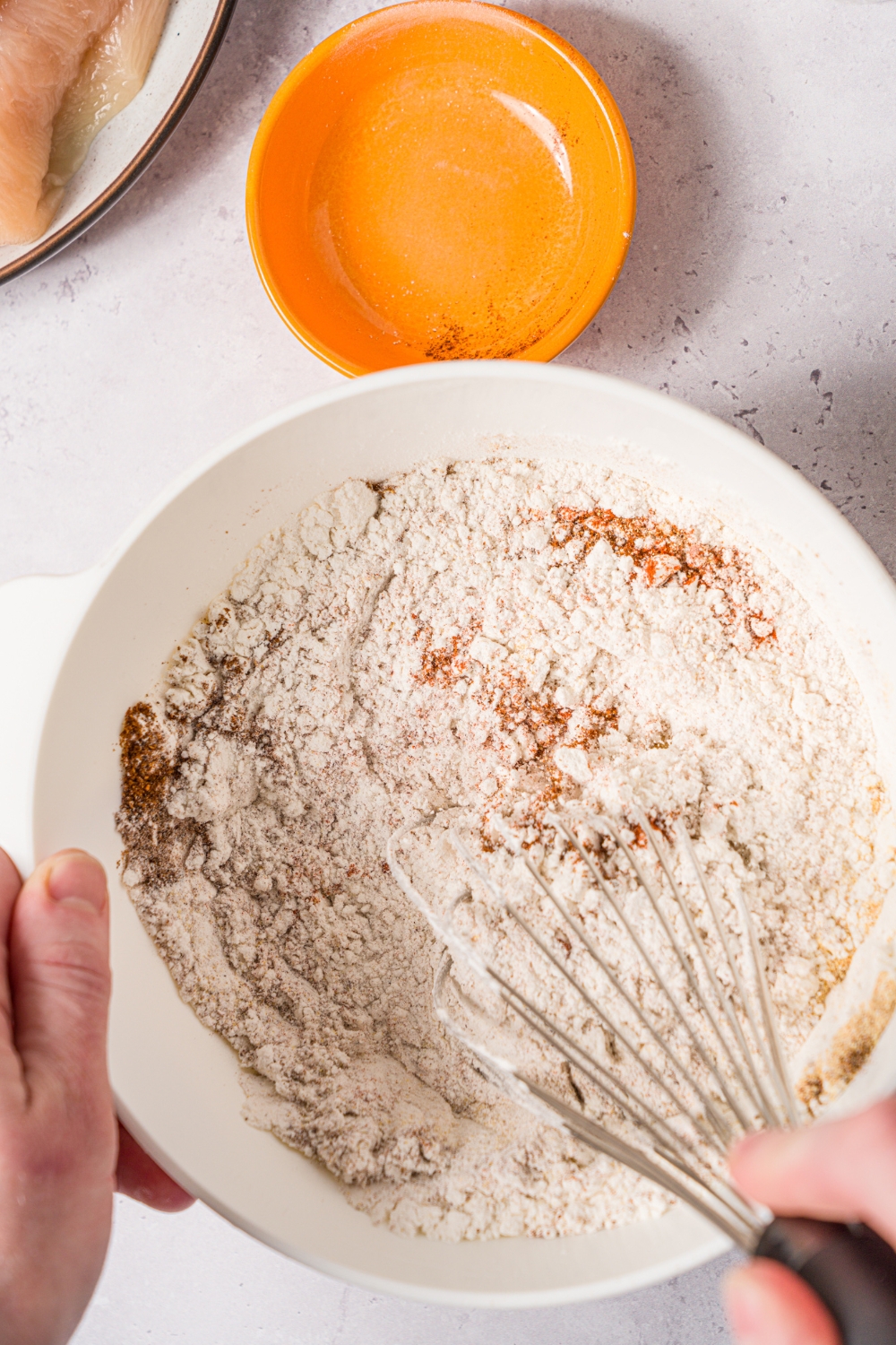 A hand whisking together a floured spice mixture in a big white bowl.
