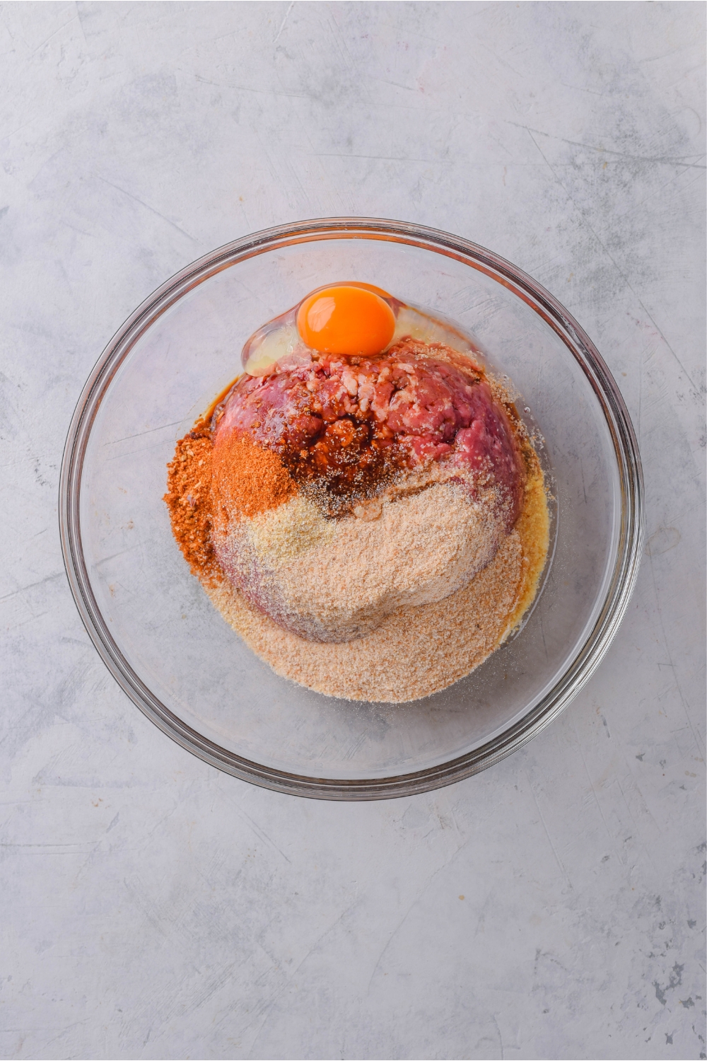 A mixing bowl with egg, seasonings, and ground beef.